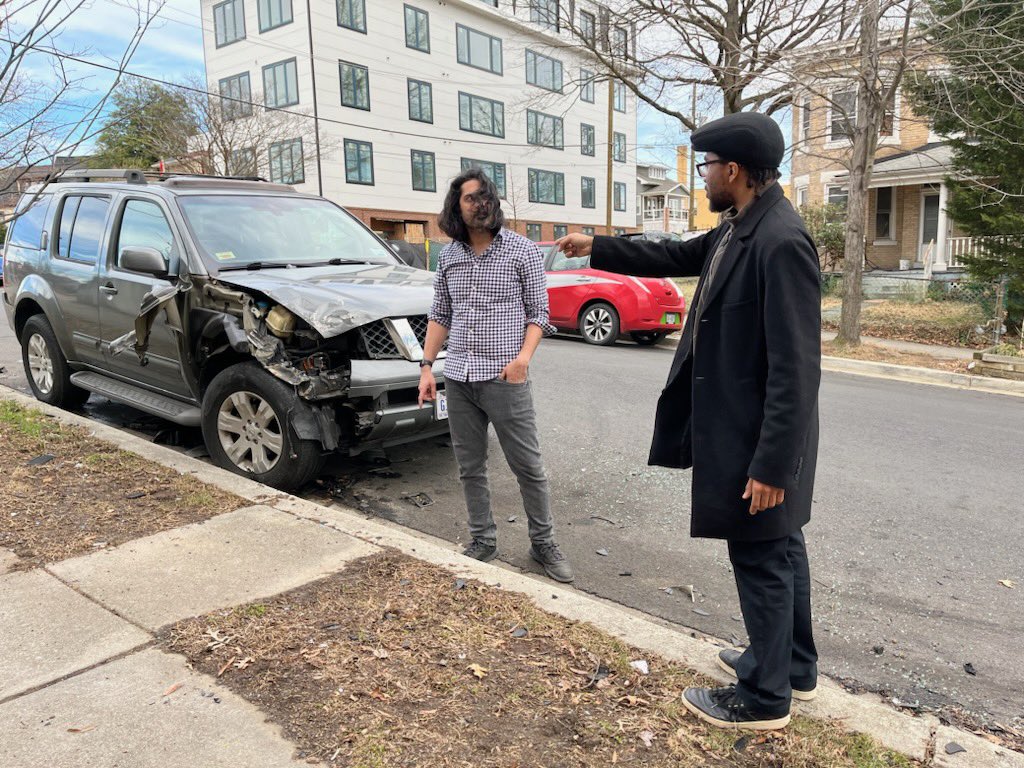 Commissioner Kapur and Mr. McKnight from Councilmember Parker's office discussing the crash in front of a damaged vehicle